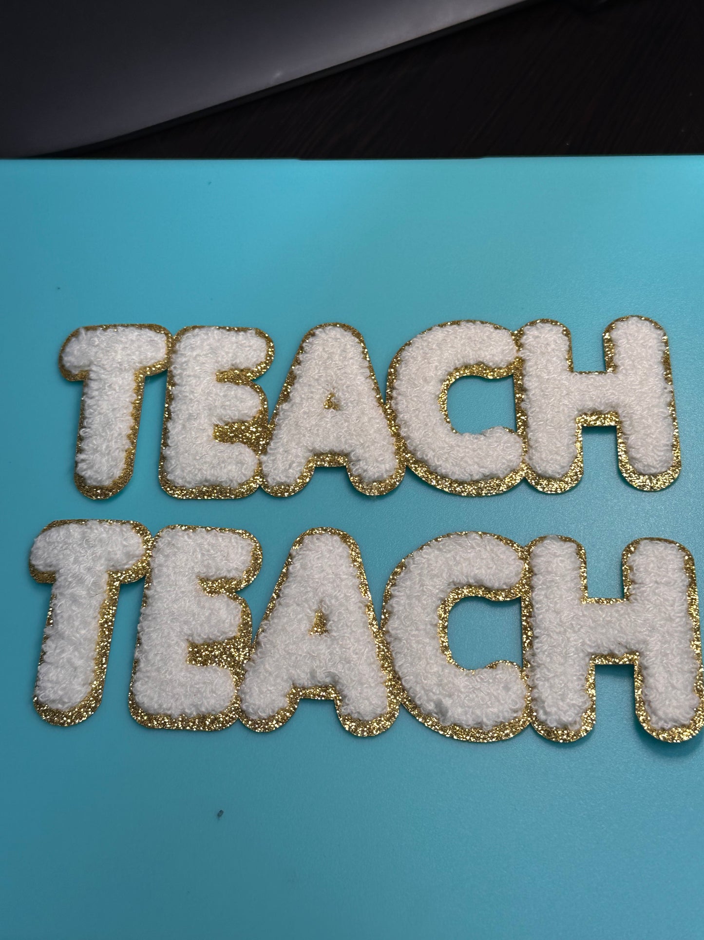 TEACH/ WHITE AND GOLD PATCH MEDIUM APPROX.  2x7 -WHITE CHENILLE AND GOLD GLITTER/ TEACHER